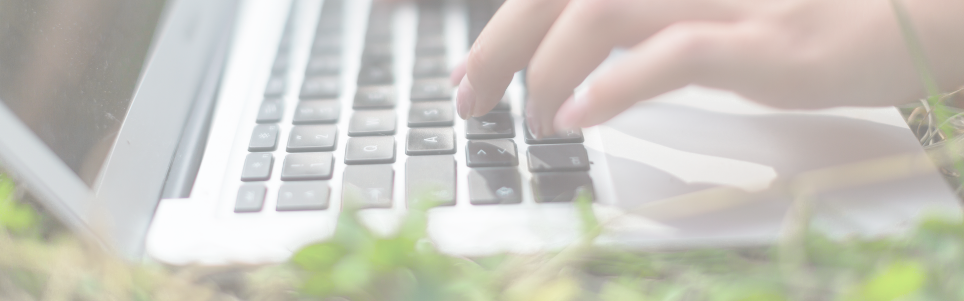 A laptop on the grass and a person's hand typing