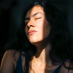 A young woman closes her eyes against the sunlight that seeps into a dark room