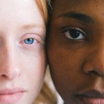 A Caucasian and African woman stand with their faces side by side