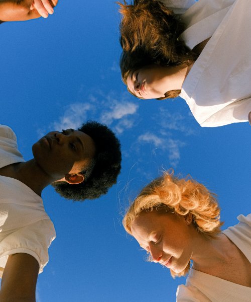 An African woman and two Caucasian women join hands while dancing in a circle outside